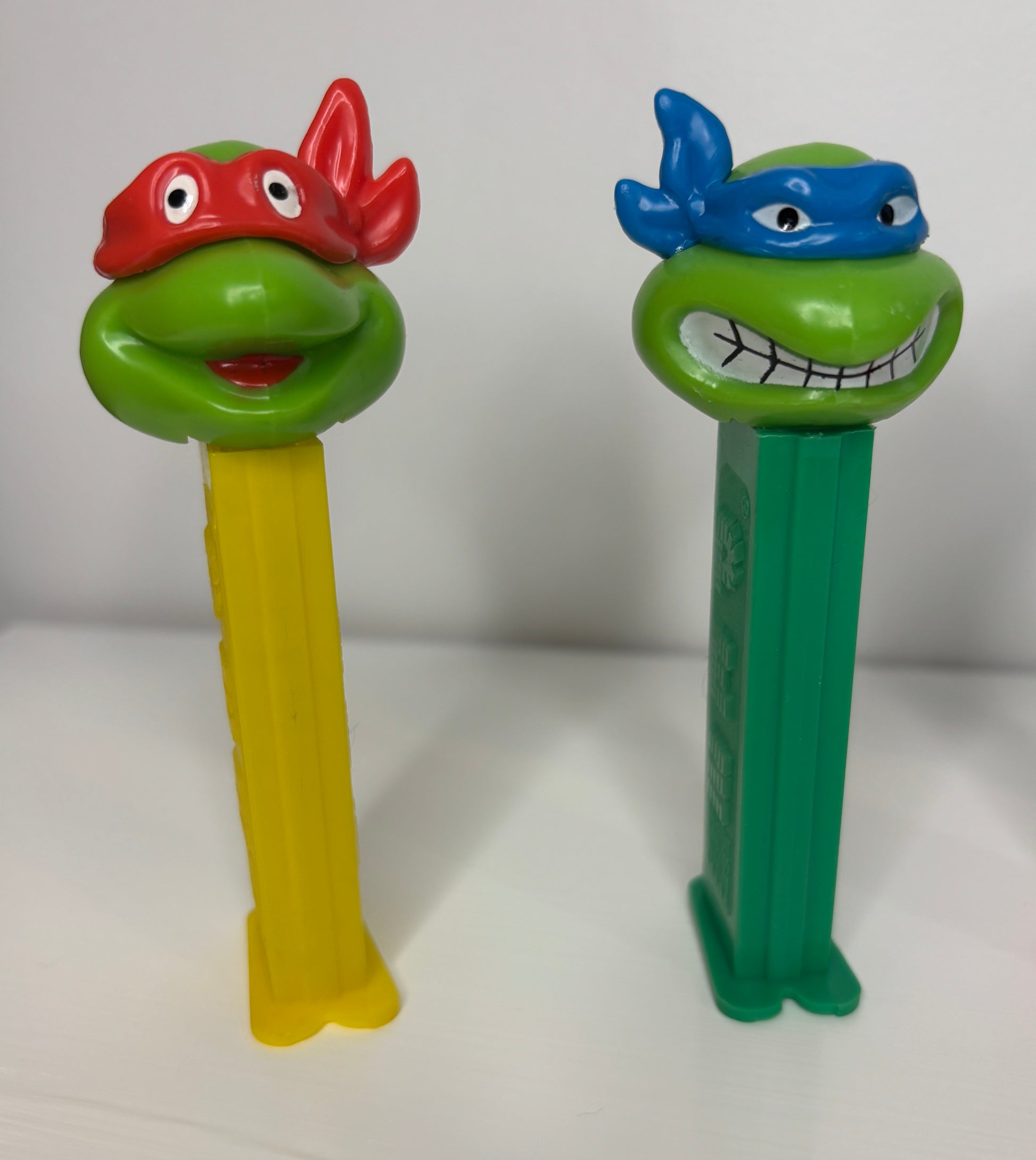 Two PEZ dispensers shaped like turtles with masks on a white background