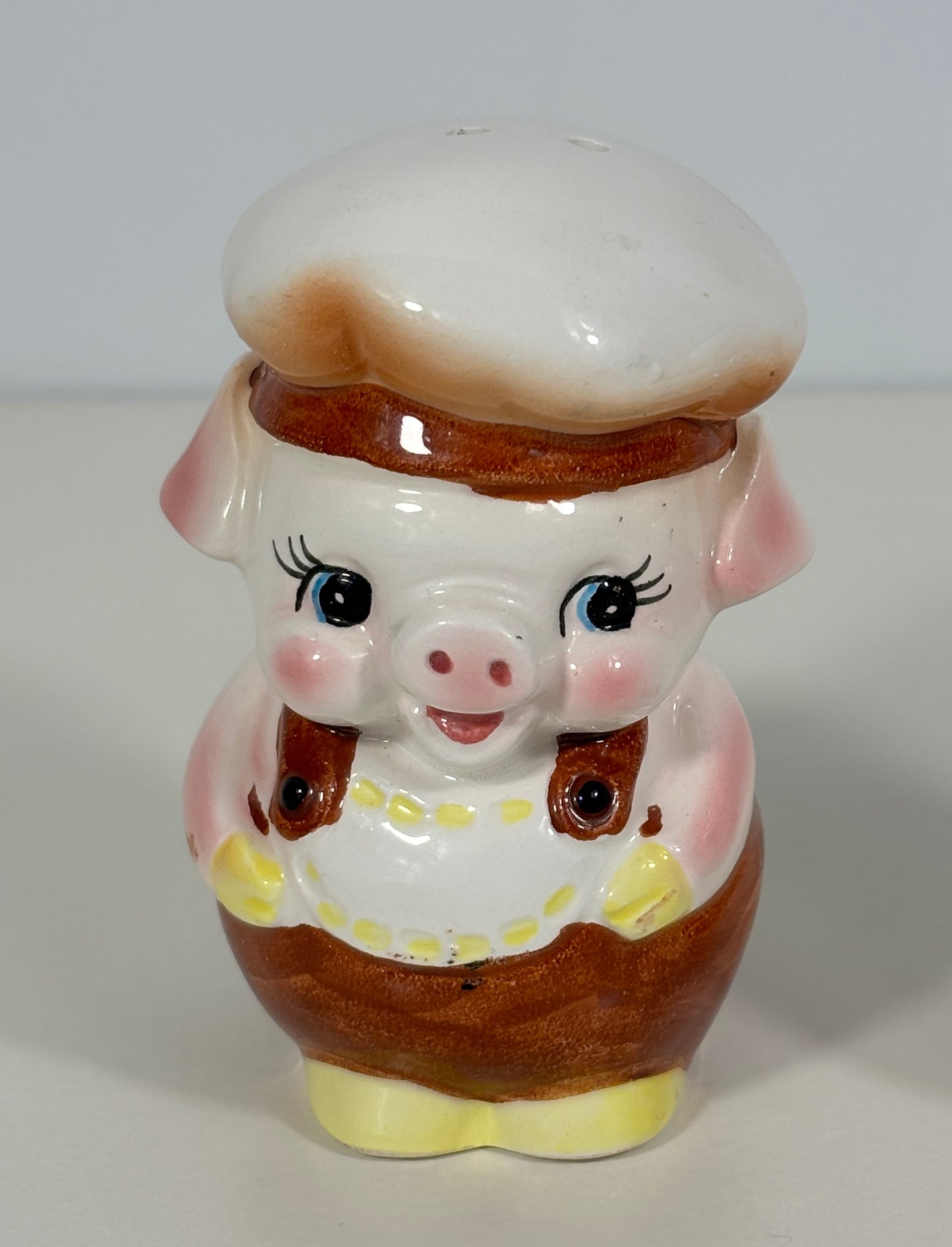 Pig-shaped ceramic pepper shaker with a chef's hat on a white background