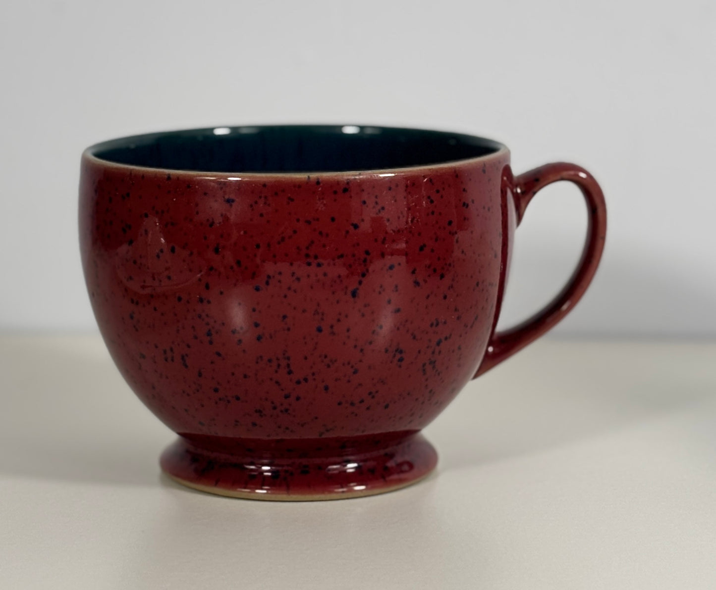 Red speckled ceramic mug on a light gray background