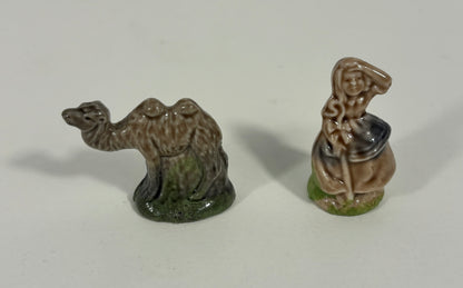 Two small glazed ceramic figurines on a plain light background: a camel standing on the left and a seated robed figure on the right.