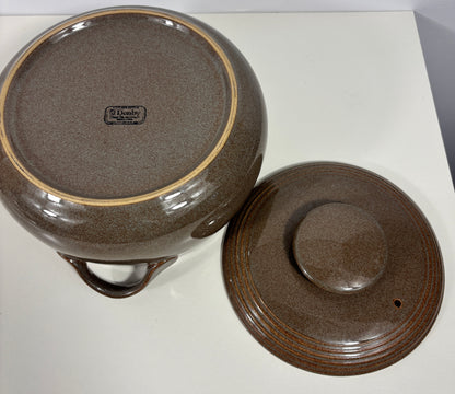 A brown speckled ceramic lidded pot or casserole dish shown from above on a white surface, with the matching lid placed beside it. A small interior brand mark is visible on the bottom of the pot.