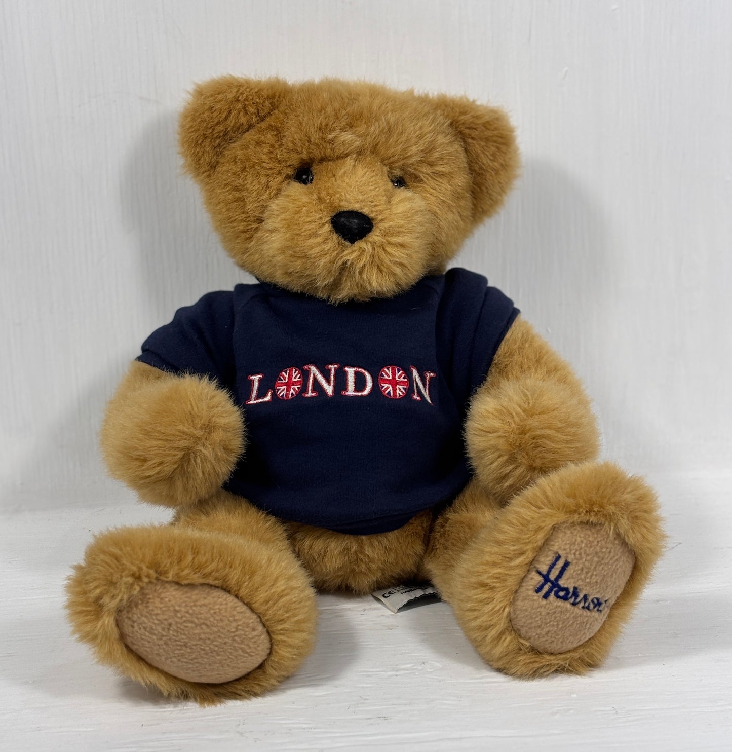 Teddy bear wearing a 'London' shirt with a Union Jack design on a white background