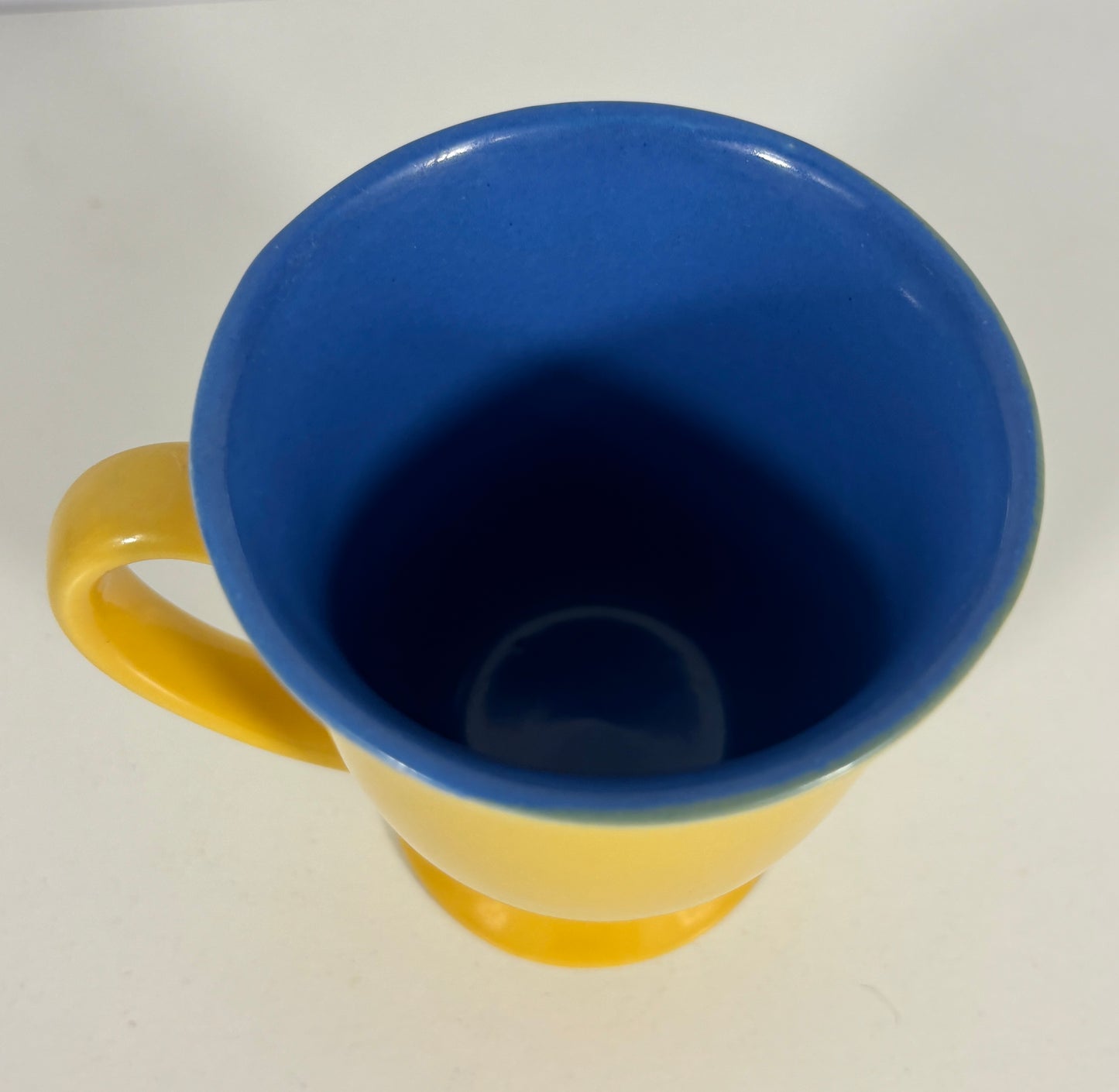 A ceramic mug with a bright yellow exterior and handle, and a contrasting deep blue interior, shown from a top-down perspective on a plain white surface.