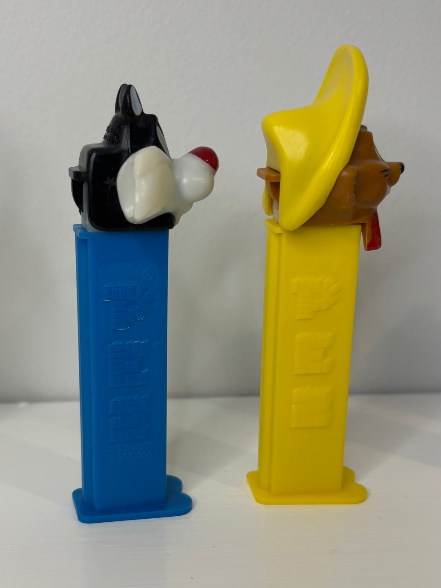 Two Pez dispensers, one blue with a black and white character and one yellow with a brown and white character, on a white background.