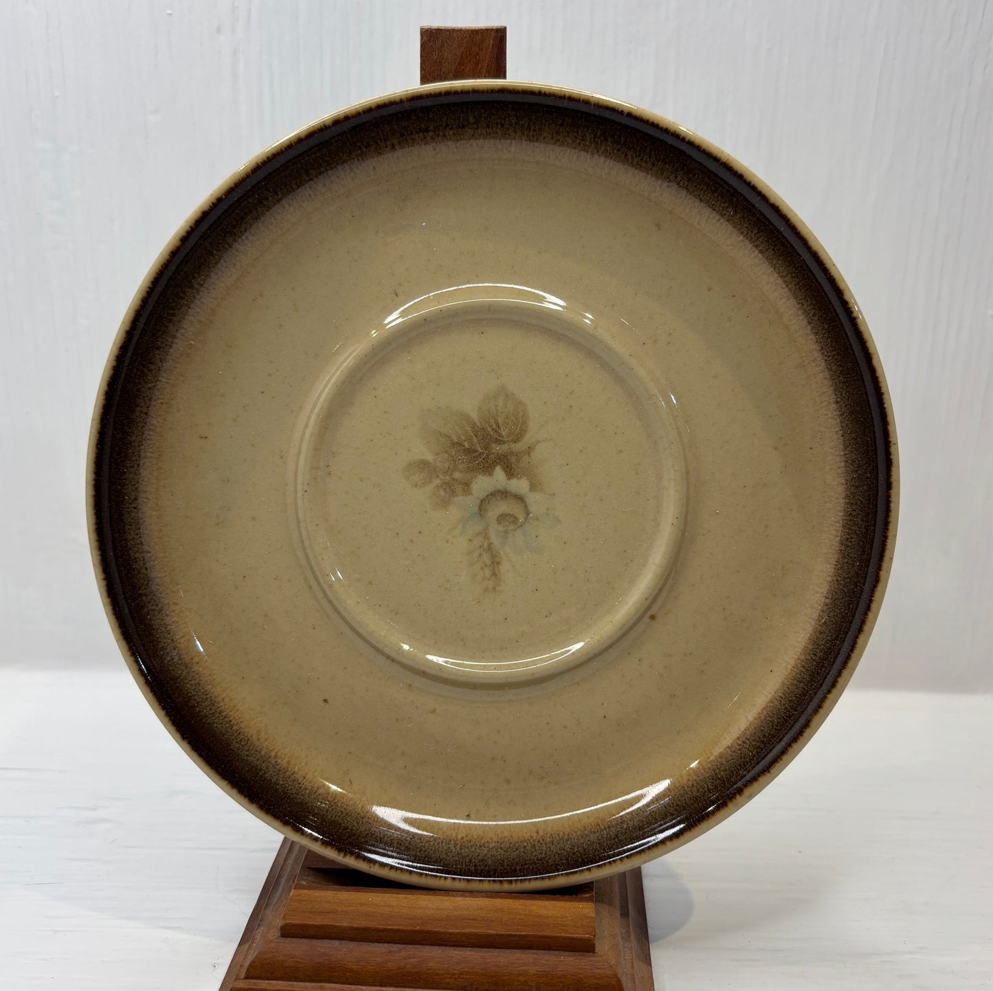Ceramic plate with a floral design on a wooden stand against a white background