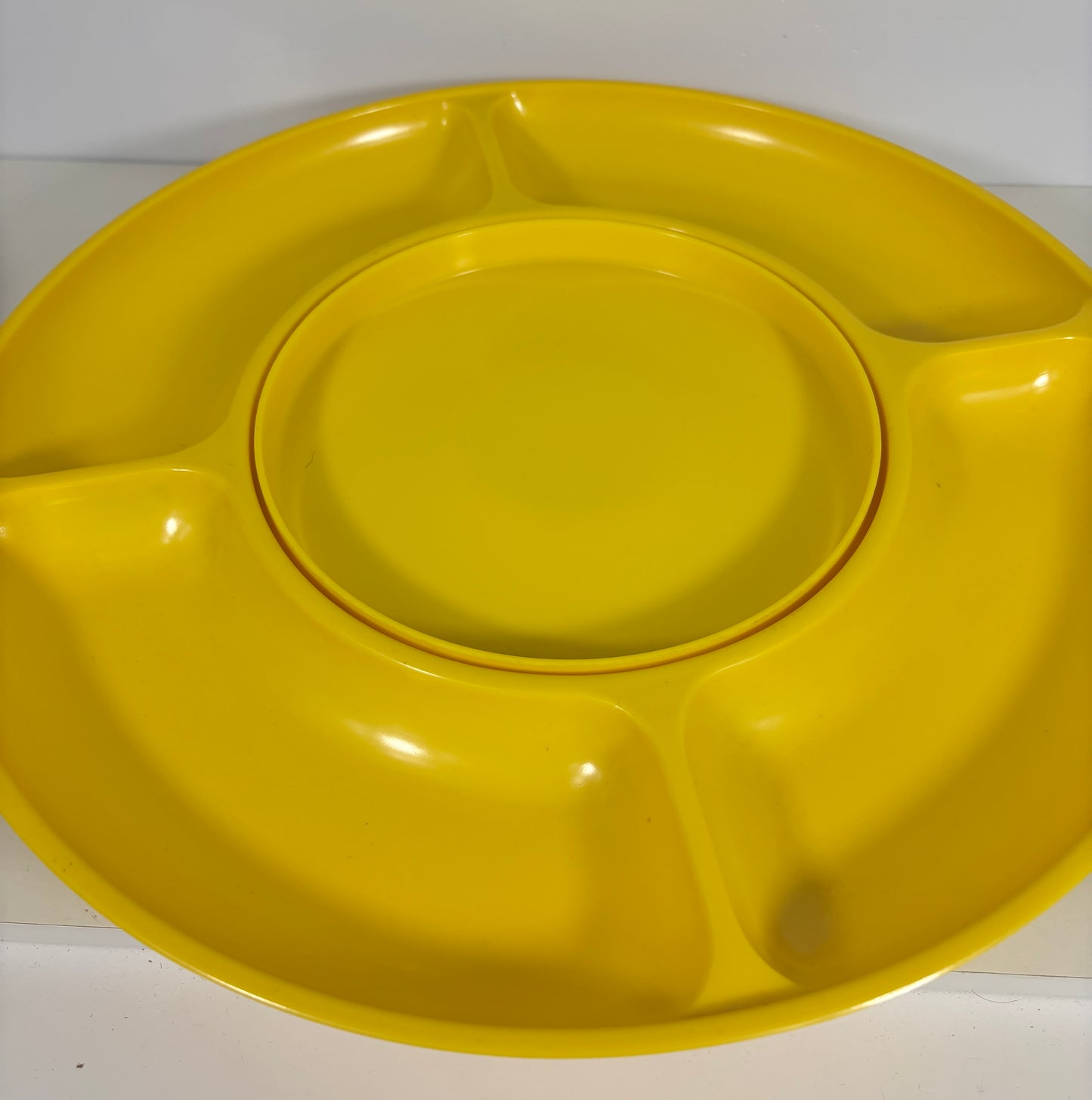 A bright yellow plastic divided plate with a central round plate that fits inside, photographed against a plain light background.