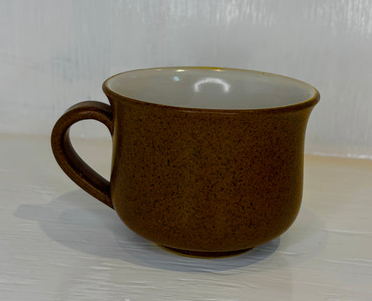 Brown ceramic mug on a white surface with a light gray background