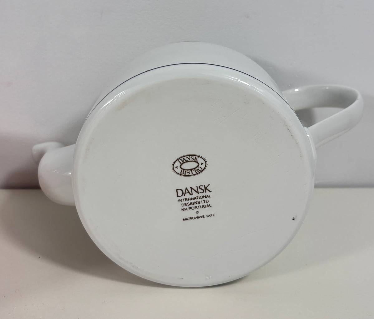 White Dansk International Designs Co. microwave safe teapot shown from the bottom, displaying the brand logo and text on the base.