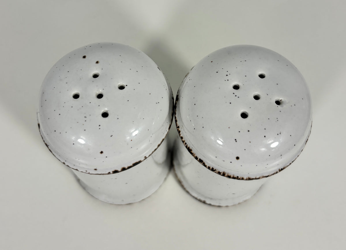 A pair of vintage white ceramic salt and pepper shakers with dark brown speckled detailing and a rustic chipped rim, shown on a plain light background.
