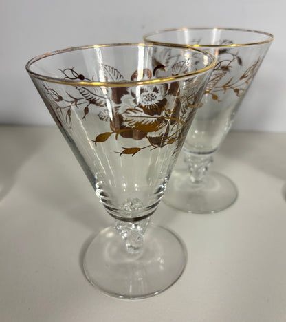 Two glass cocktail glasses with gold floral patterns on a white surface.