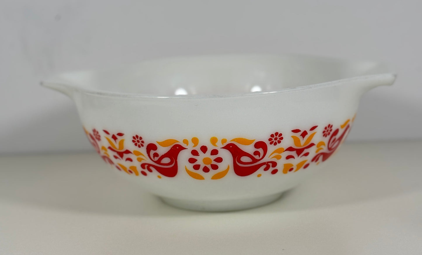 White bowl with red and orange floral and bird pattern on a white background