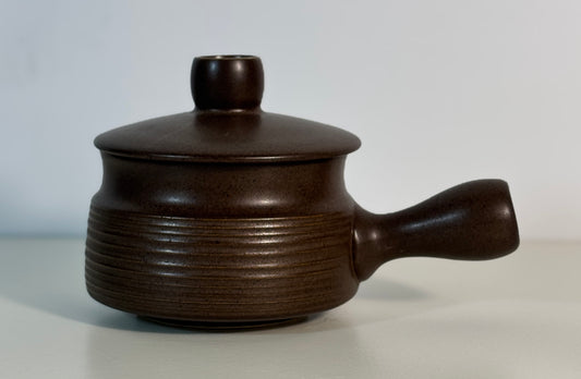 Dark brown ceramic pot with lid and handle on a light gray background