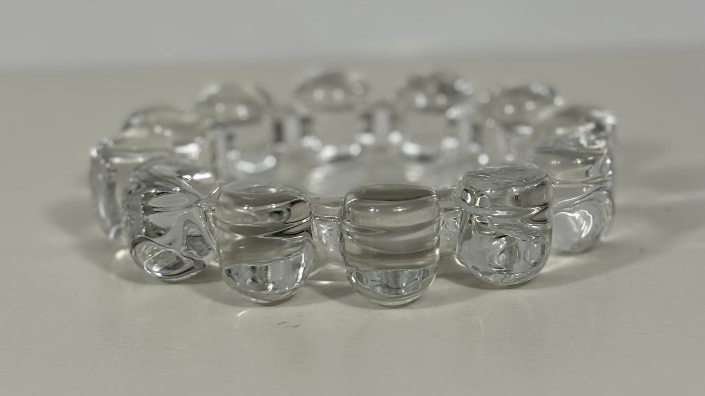 A clear glass stretch bracelet made of linked rounded beads, photographed on a plain light surface.
