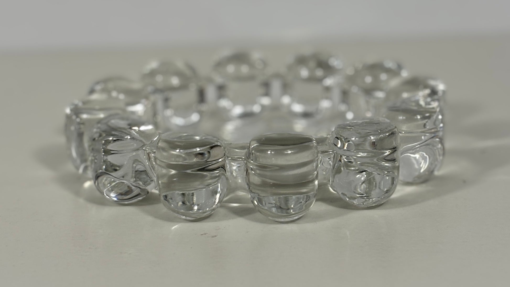 A clear glass stretch bracelet made of linked rounded beads, photographed on a plain light surface.