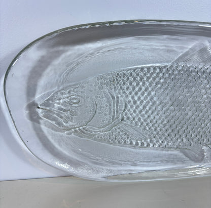 A clear glass dish featuring an embossed fish design, photographed from a top-down angle on a white background.