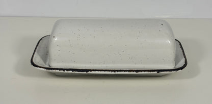 A white speckled ceramic butter dish with a matching lid, featuring a rustic black rim, set against a plain off-white background.