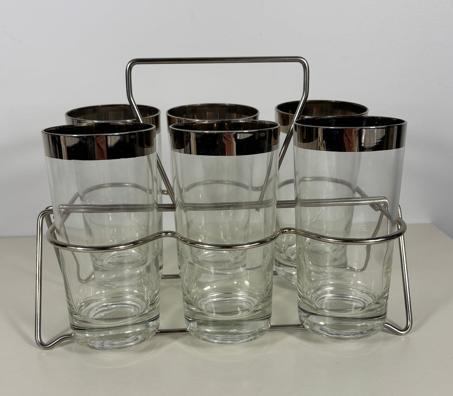 Set of six clear glasses with silver rims in a metal holder on a white background