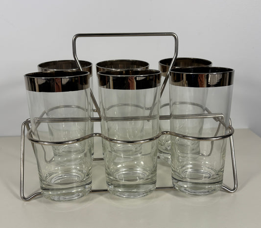 Set of six clear glasses with silver rims in a metal holder on a white background