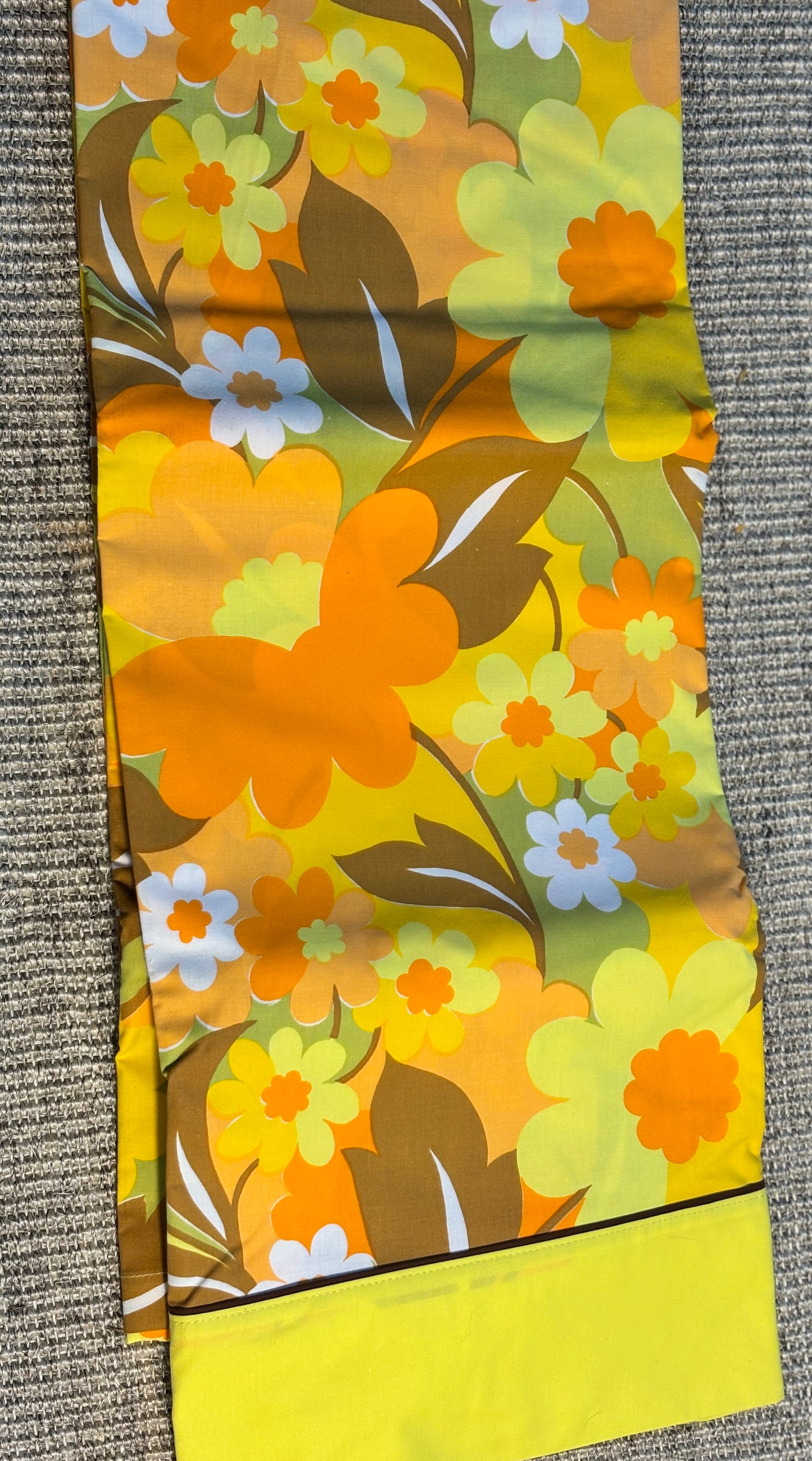 Floral patterned fabric with orange, yellow, and green colors on a textured surface.