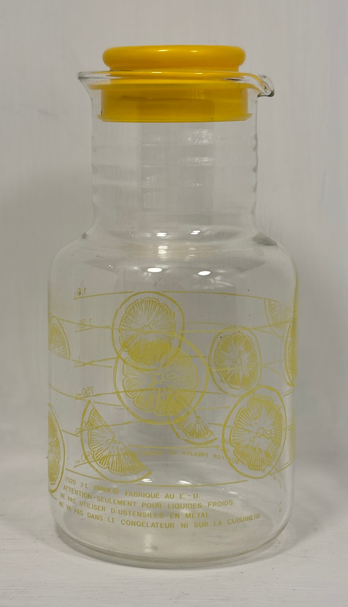 Clear glass bottle with yellow cap and lemon illustrations on a white background