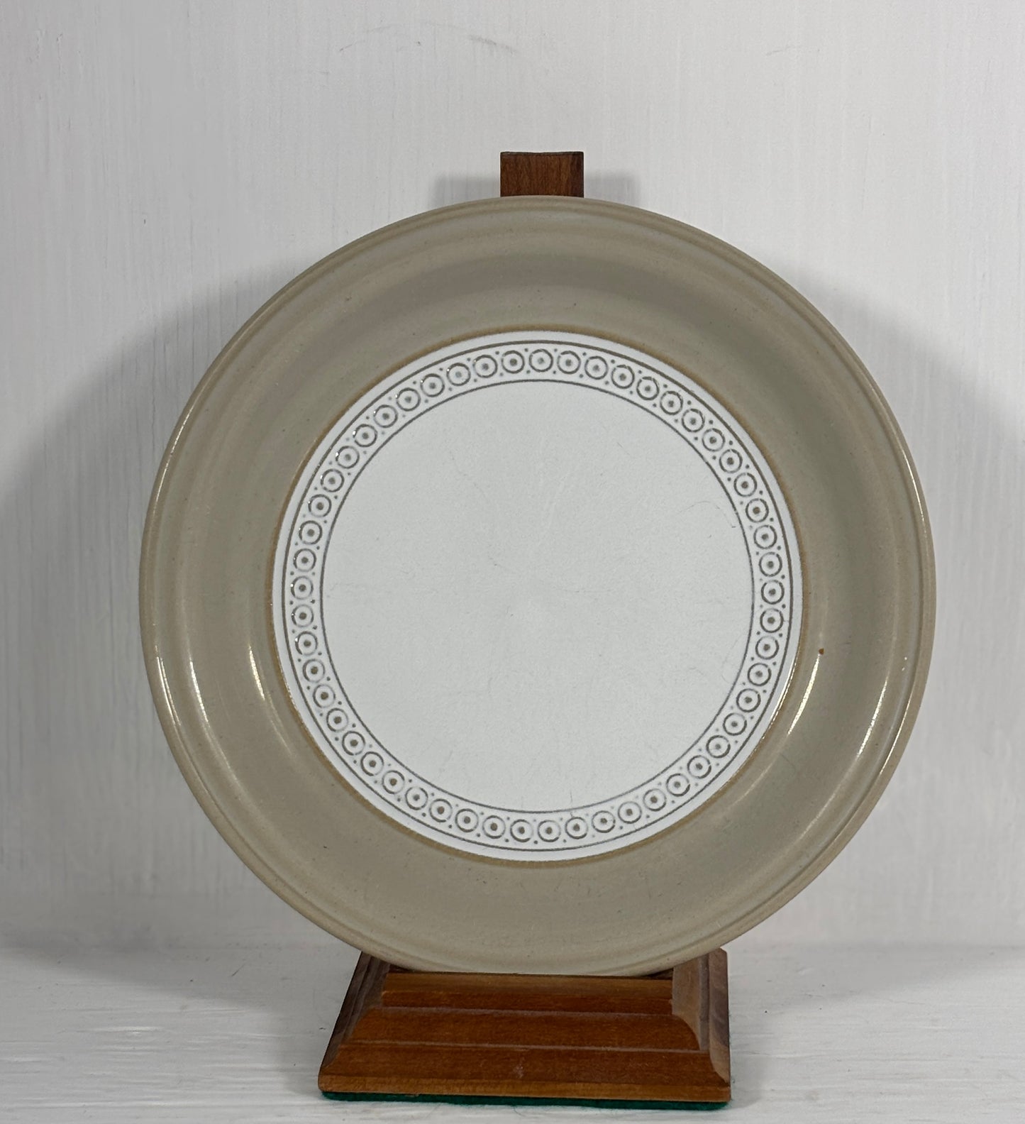 Round ceramic plate with decorative rim on a wooden stand against a plain background