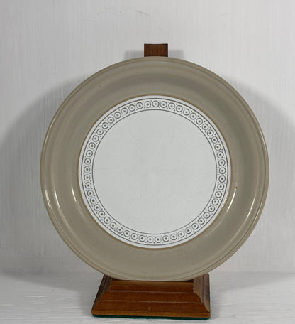 Round ceramic plate with decorative rim on a wooden stand against a plain background