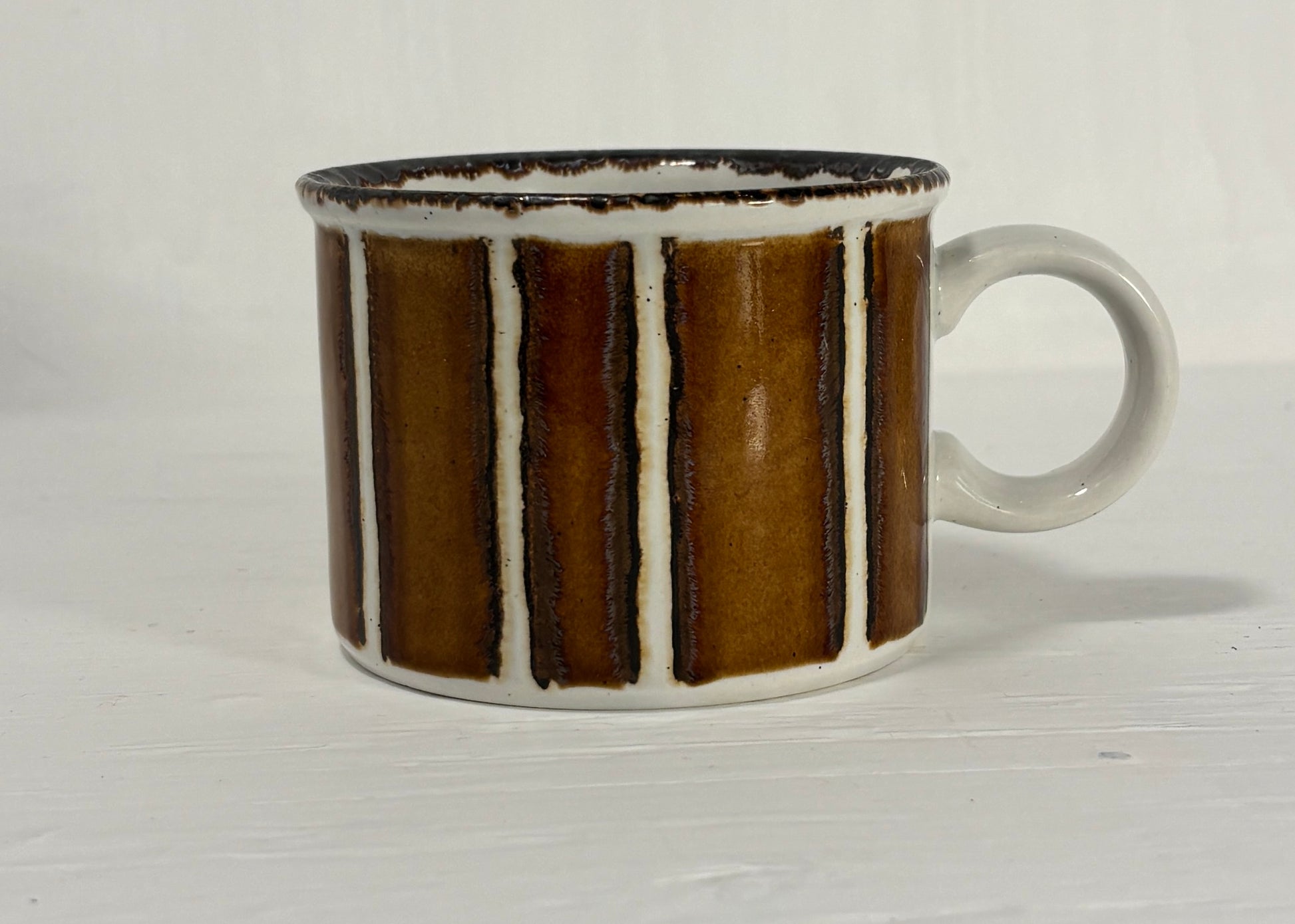 Ceramic mug with brown and white striped design on a light wooden surface