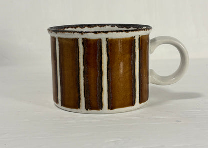 Ceramic mug with brown and white striped design on a light wooden surface