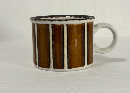 Ceramic mug with brown and white striped design on a light wooden surface