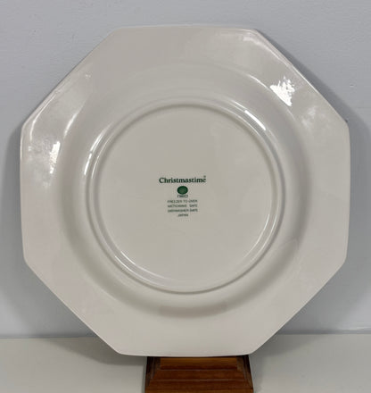 An octagonal white ceramic Christmas plate displayed on a small wooden stand against a light gray wall.
