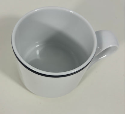 A white ceramic mug with a single black stripe around the rim, shown from a top-down angle on a light off-white background.