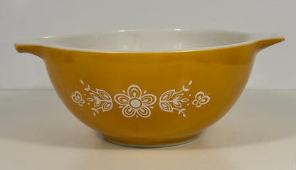 A yellow glass mixing bowl with a white interior and white floral pattern decoration on the exterior, set against a plain light background.