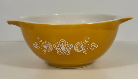 A yellow glass mixing bowl with a white interior and white floral pattern decoration on the exterior, set against a plain light background.