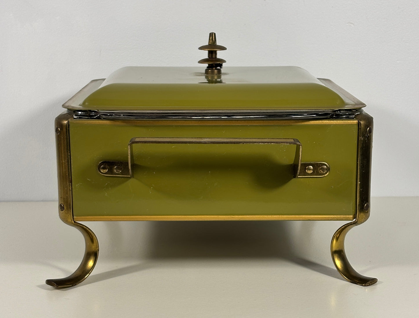 An antique-style lidded serving box or chafing dish with a muted olive green enamel finish and brass-toned metal legs, handle, and trim, set against a plain white background.