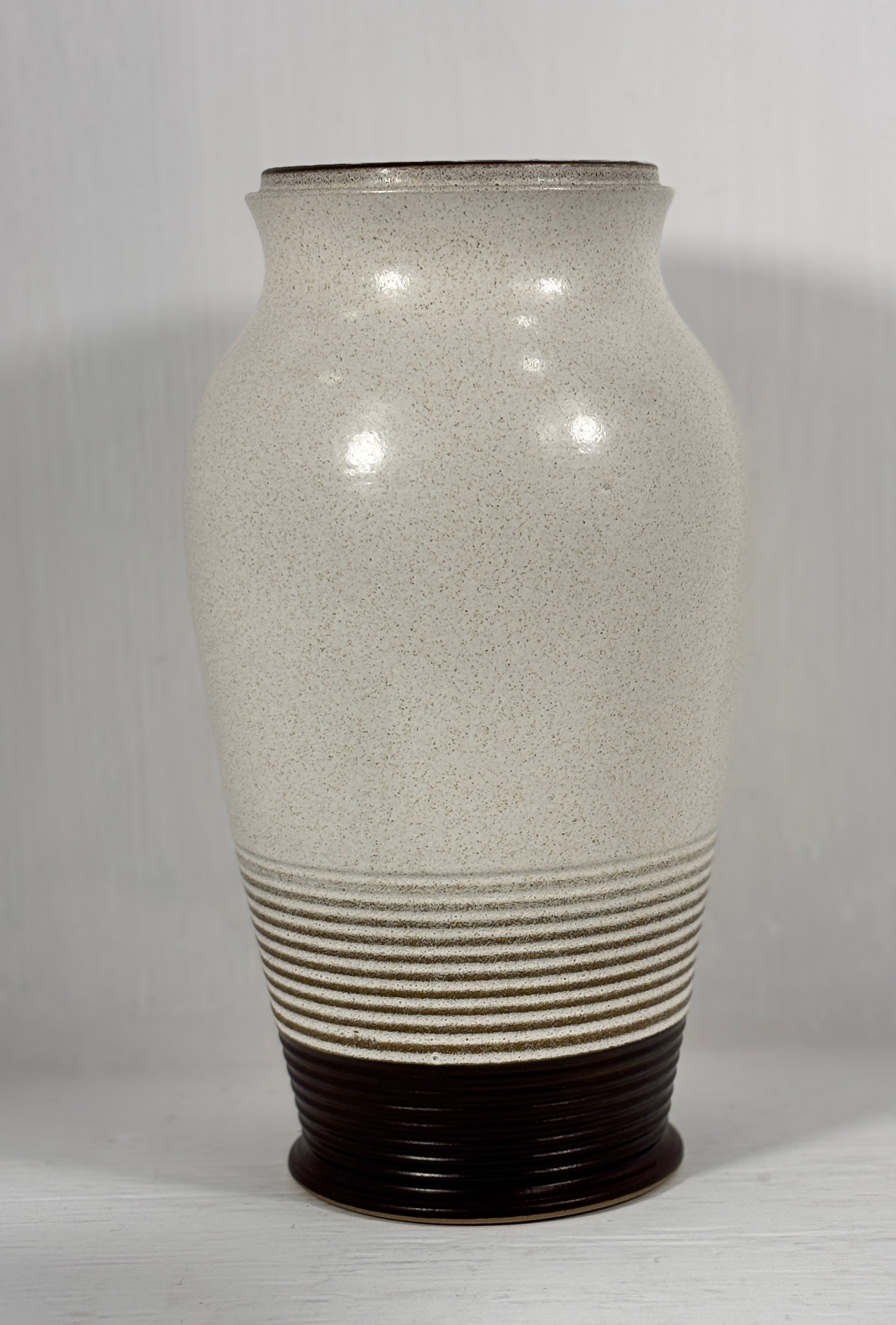 stoneware vase with textured surface and brown base on a plain background