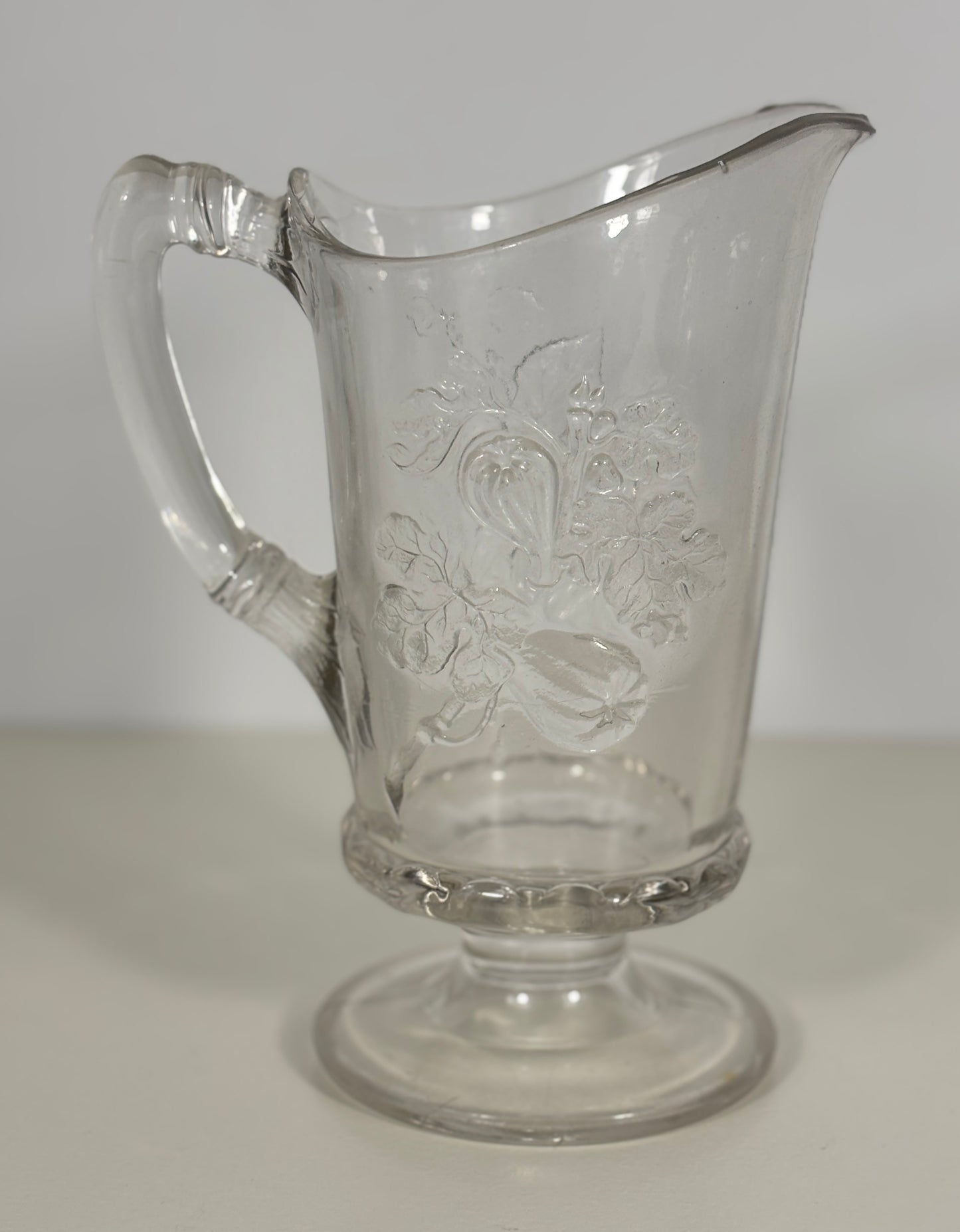 Clear glass pitcher with embossed design on a white background