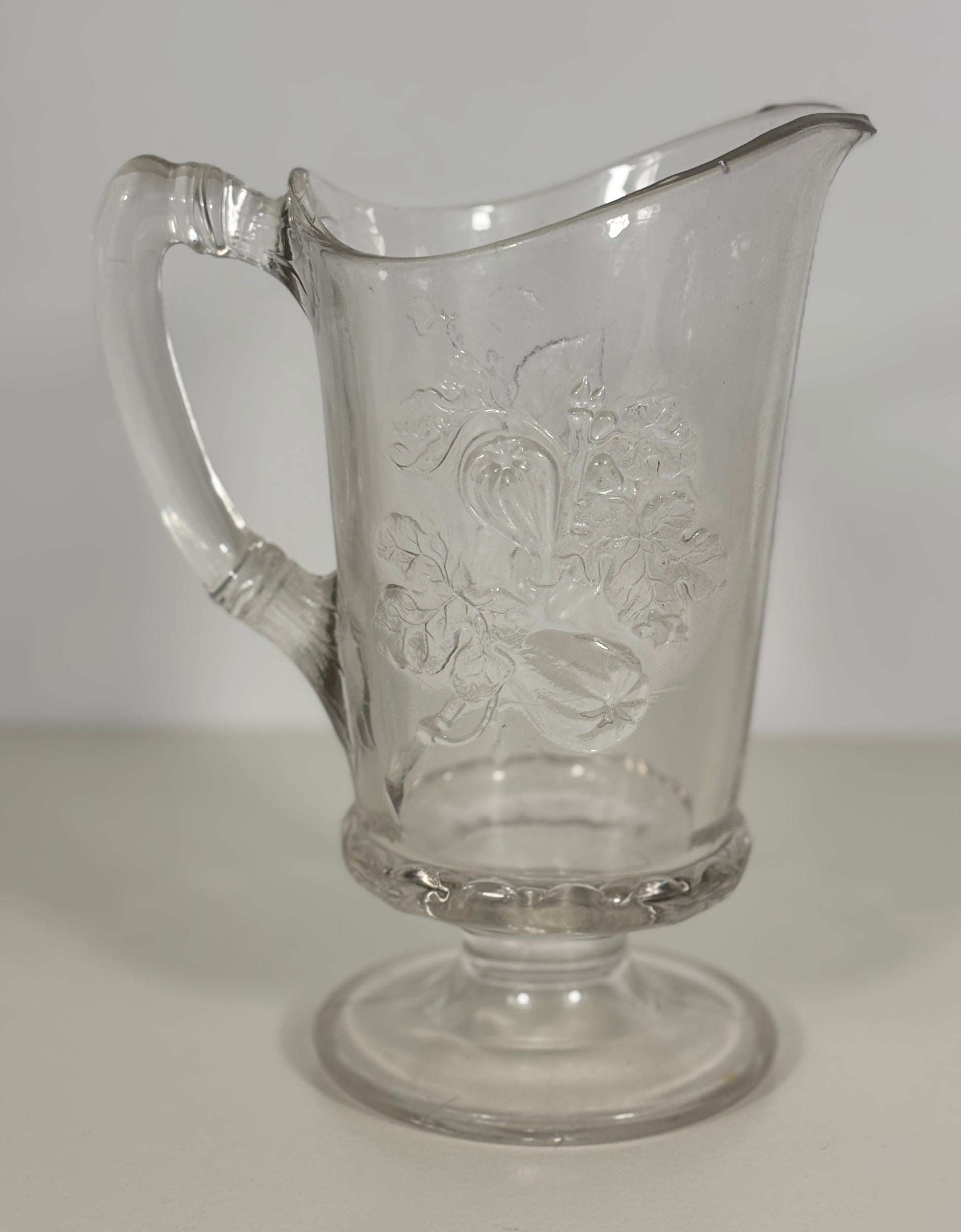 Clear glass pitcher with embossed design on a white background
