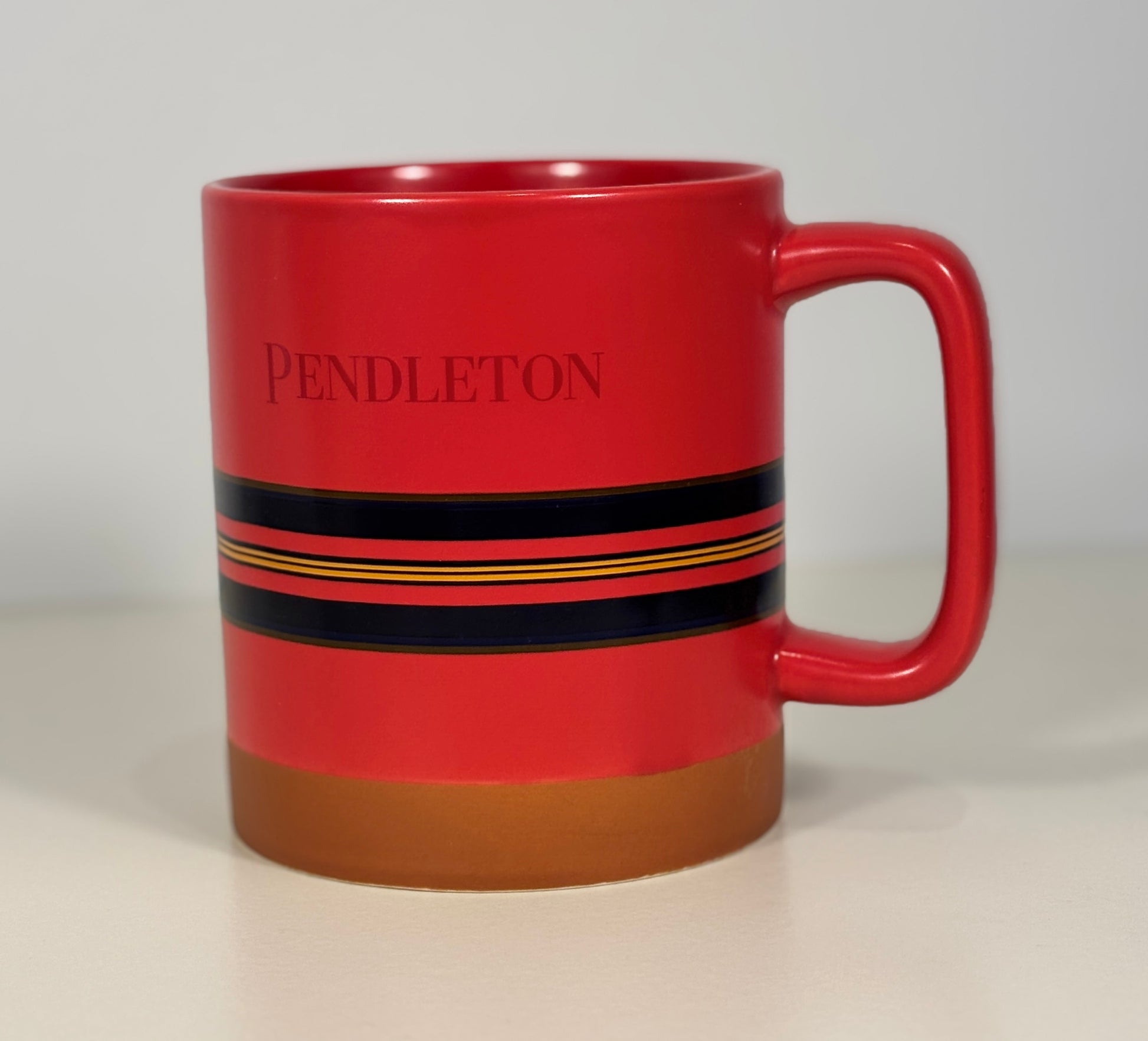 Red mug with black and brown stripes and 'Pendleton' branding on a light gray background