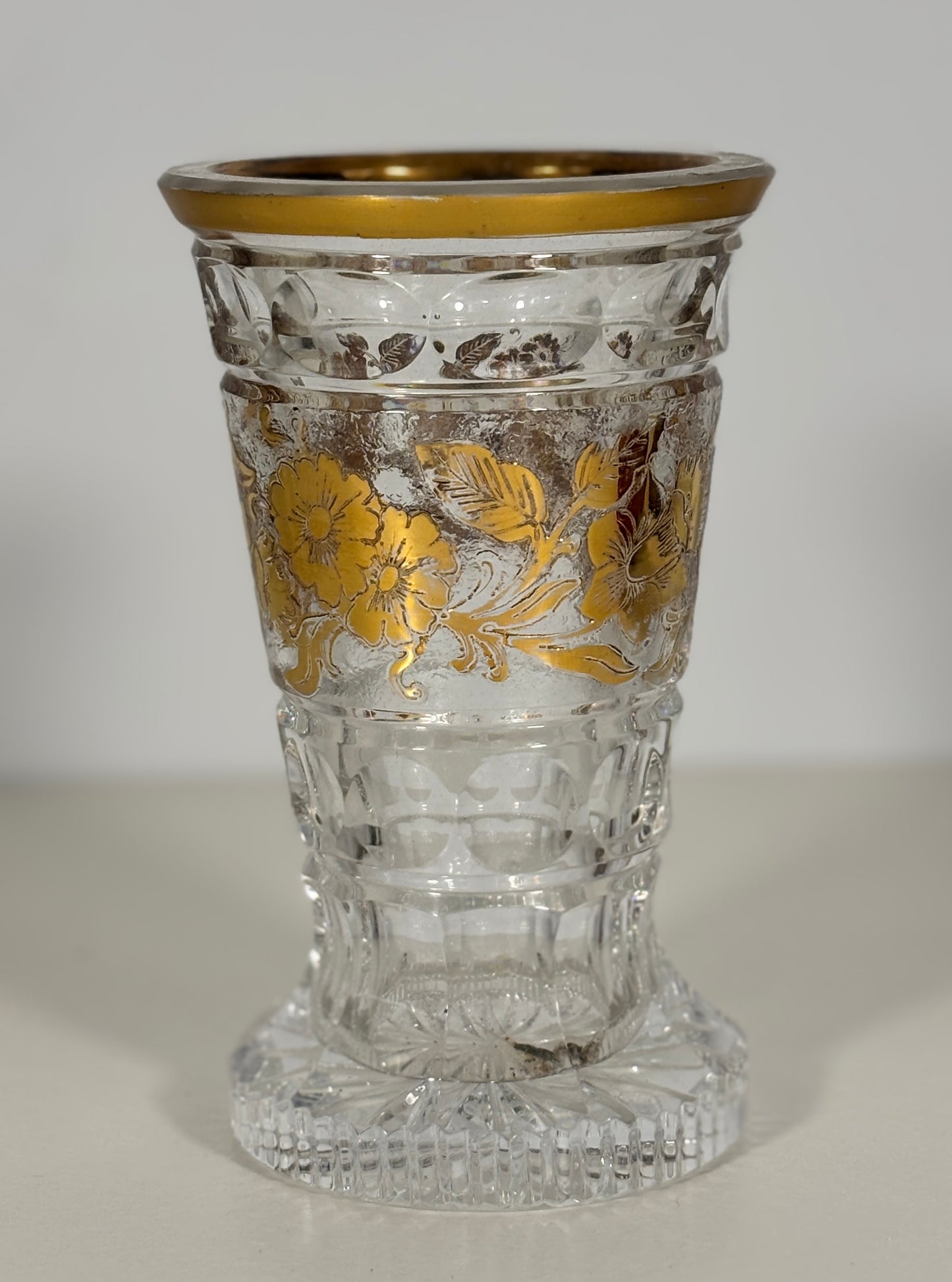 Decorative glass vase with gold floral patterns and a gold rim on a white background