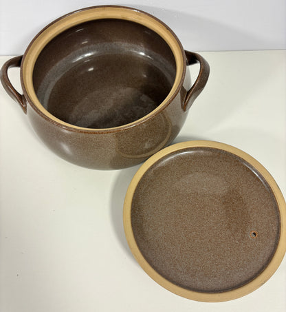 A brown ceramic lidded pot with two side handles and a matching lid placed beside it on a white surface.