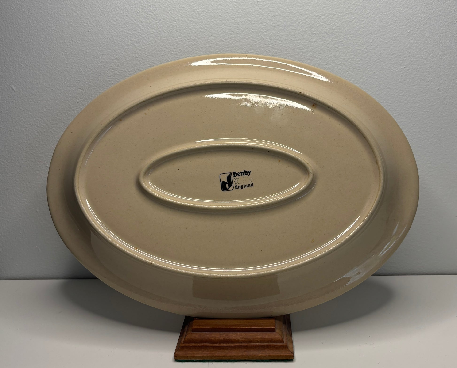 Beige ceramic platter with a visible brand logo on a gray background