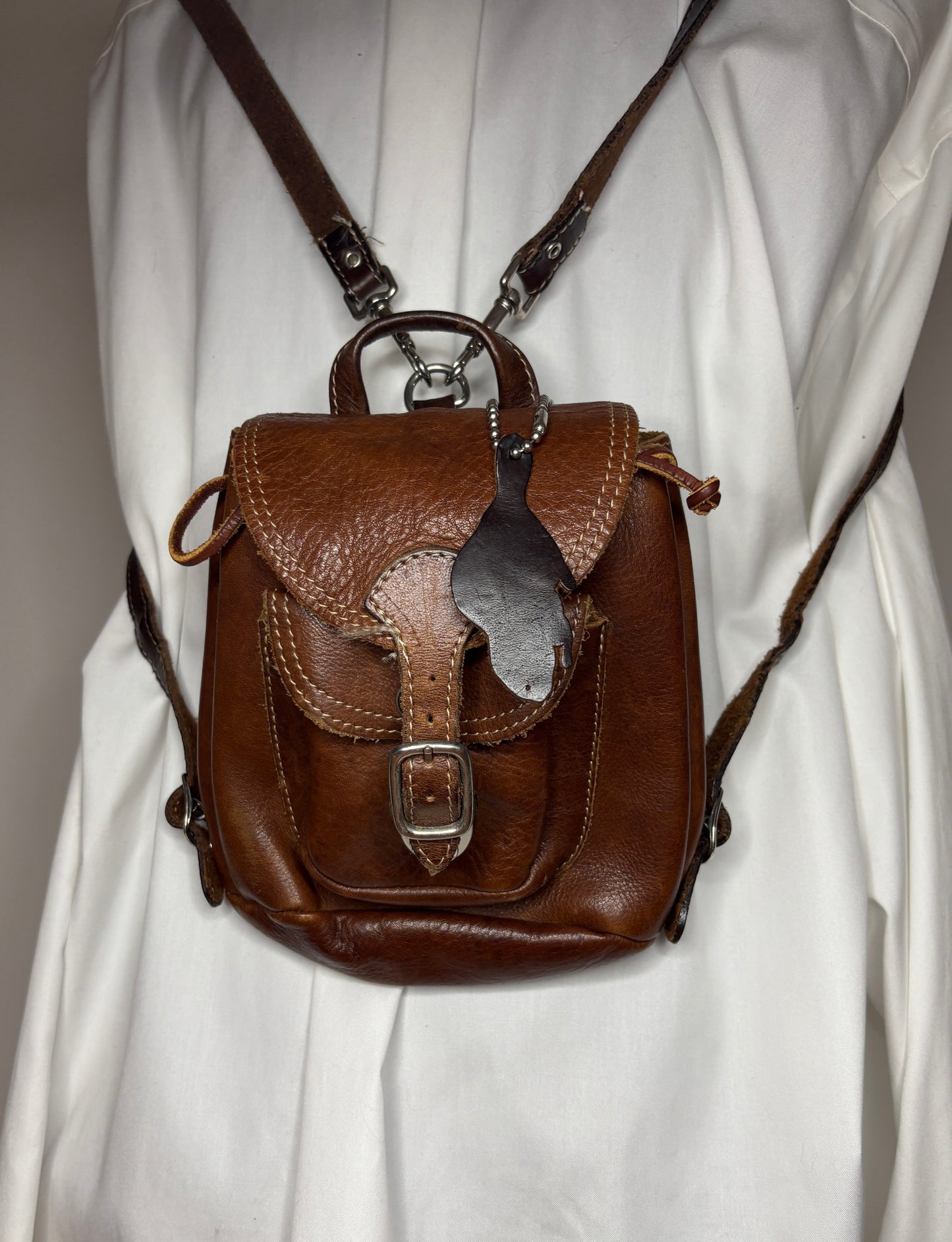 Brown leather backpack with decorative flap on a white background
