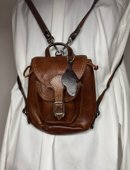 Brown leather backpack with decorative flap on a white background