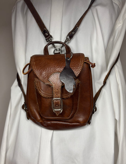 Brown leather backpack with decorative flap on a white background