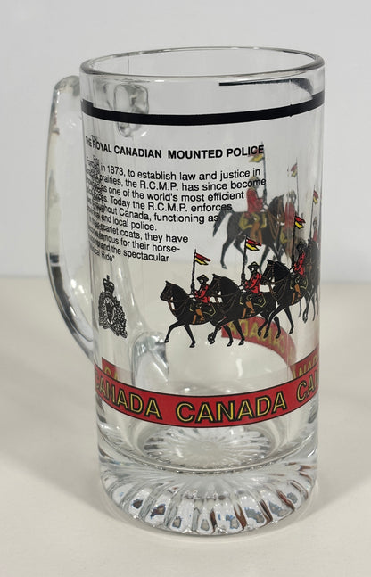 A clear glass handleless mug with embossed text and graphics of the Royal Canadian Mounted Police, including a black horse-and-rider illustration and a red band reading 'CANADA CANADA'.
