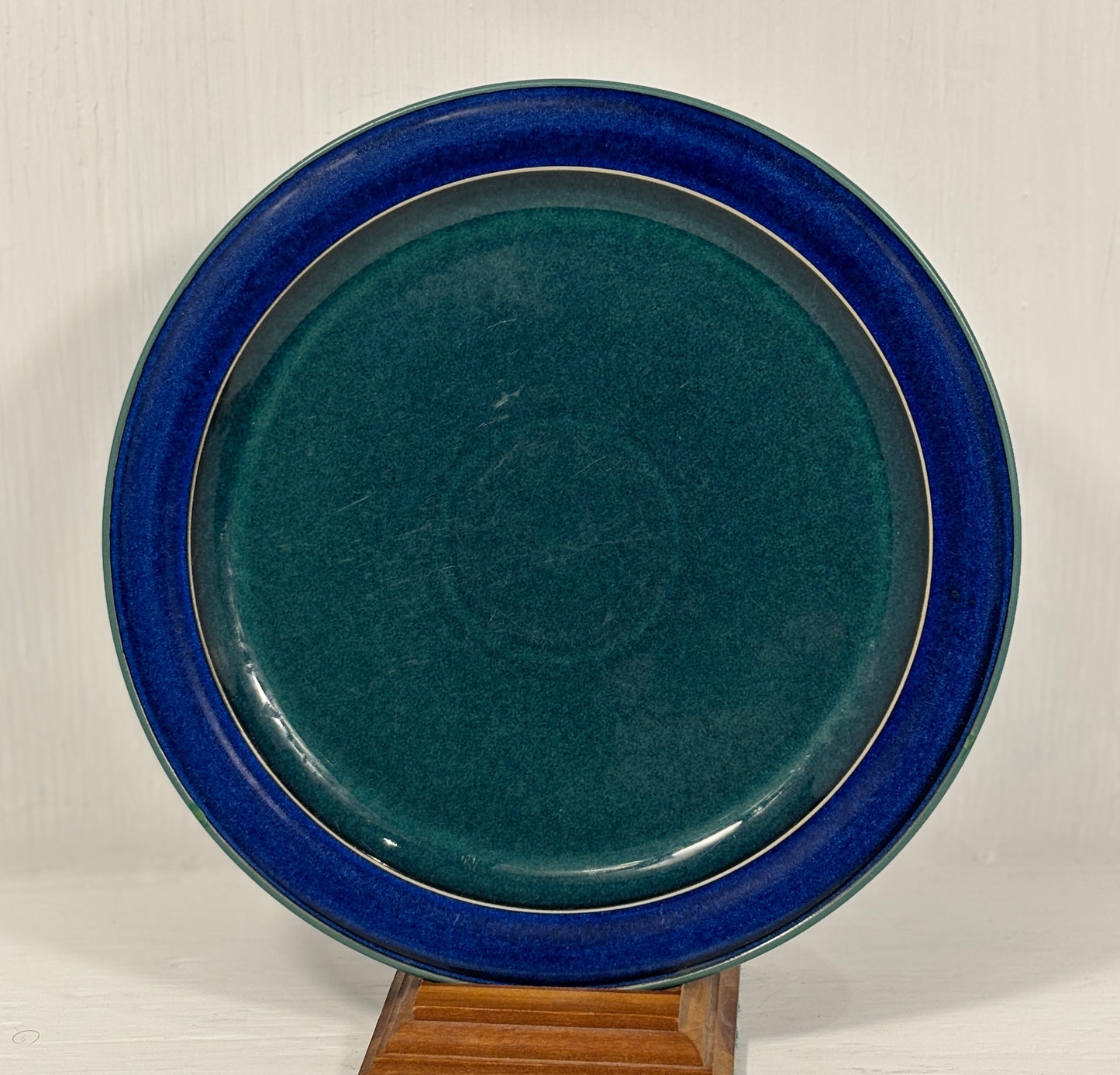 green ceramic plate with blue rim on a wooden stand against a white background