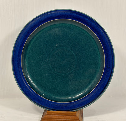 green ceramic plate with blue rim on a wooden stand against a white background