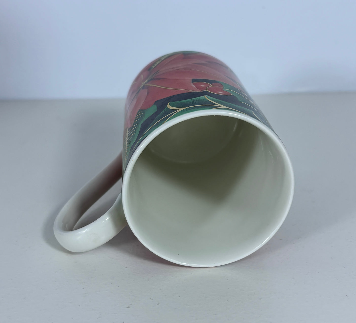 A white ceramic mug with a colorful floral wrap-around design, shown lying on its side on a light gray surface against a white background.
