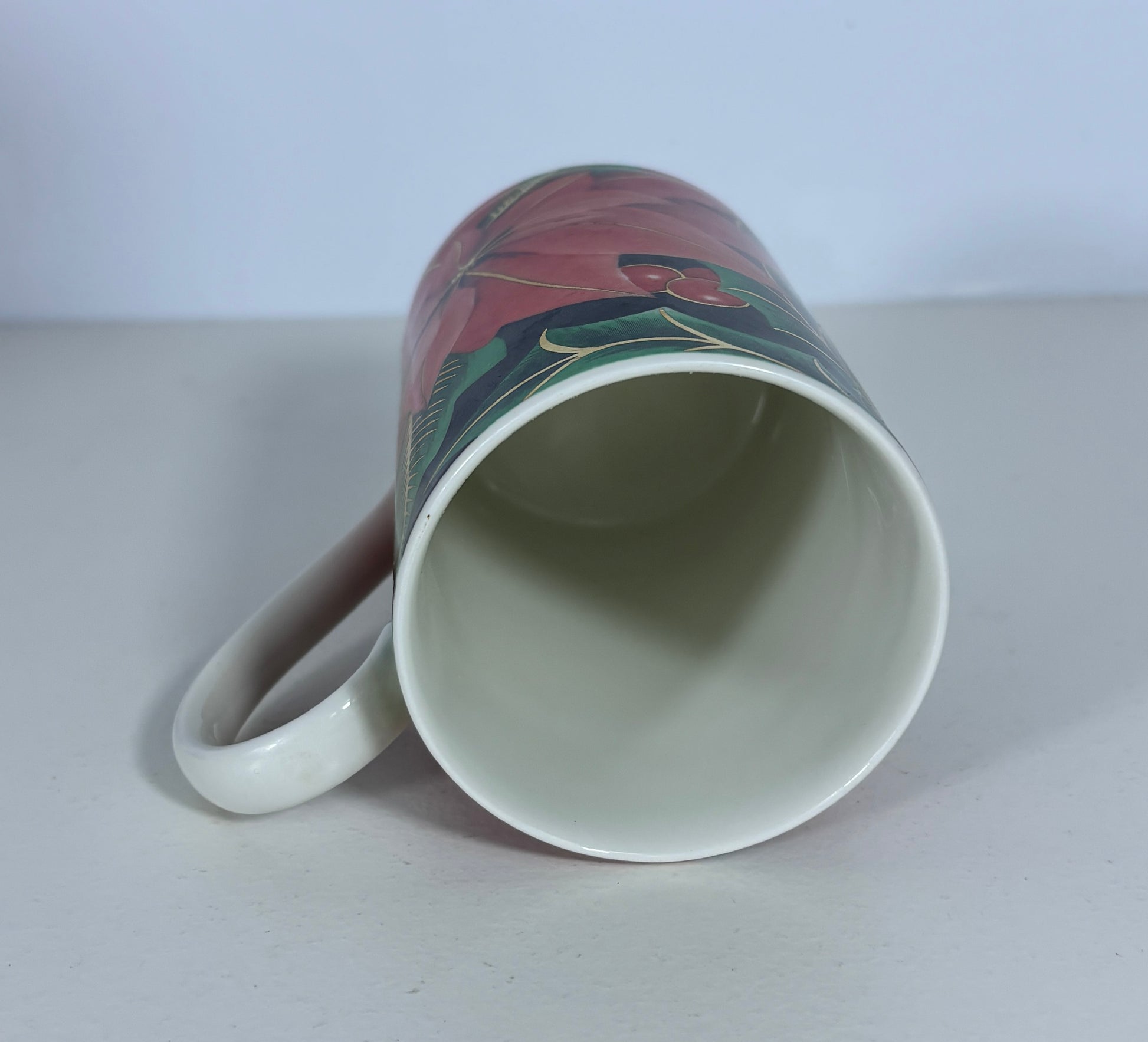 A white ceramic mug with a colorful floral wrap-around design, shown lying on its side on a light gray surface against a white background.