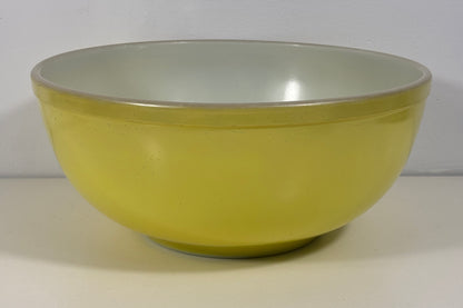 A round mixing bowl with a pale yellow exterior and a light gray interior, shown against a neutral off-white background.